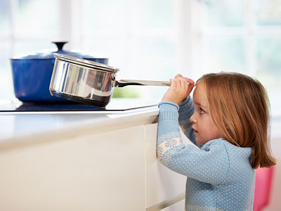 Ein kleines Mädchen, das einen Kochtopf auf einer Küchenzeile betrachtet.