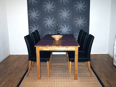 Ein Essbereich mit einem hölzernen Tisch, sechs schwarzen Stühlen und einer dekorativen Wand mit floralem Muster.
