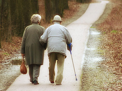 Ein älteres Paar geht Hand in Hand auf einem Weg durch die Natur.