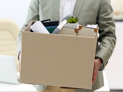 Eine Person hält einen Karton mit Büromaterialien und einer Pflanze.