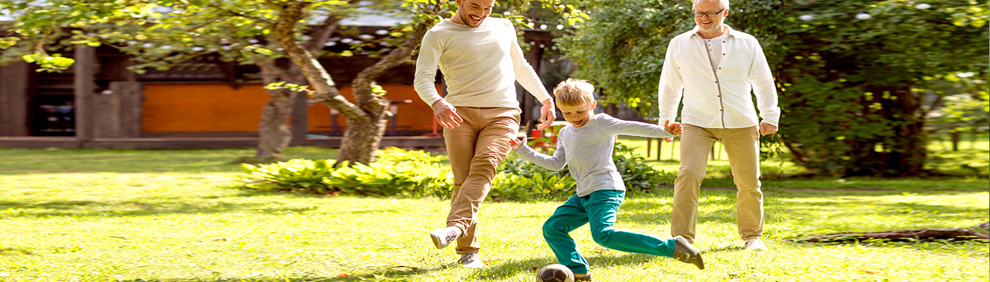 Ein Junge spielt mit einem Ball im Garten, während zwei Erwachsene ihm zuschauen und ihn anfeuern.