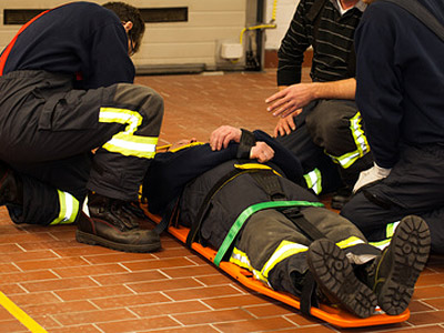 Menschen in Schutzkleidung helfen einer Person auf einer Trage in einem Ausbildungs- oder Rettungsszenario.
