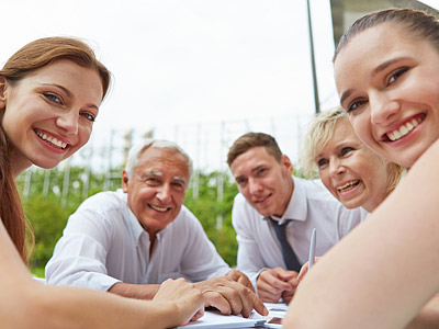 Eine Gruppe von fünf Personen lächelt und sitzt um einen Tisch im Freien.
