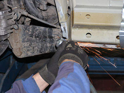 Ein Mechaniker schneidet Metall unter einem Fahrzeug und erzeugt Funken.