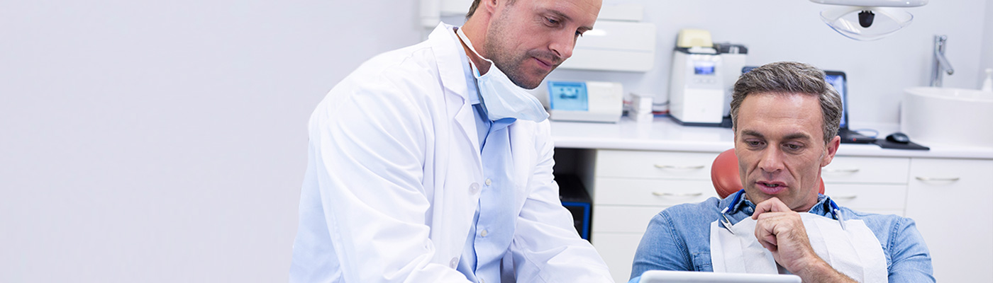 Ein Zahnarzt erklärt einem Patienten etwas auf einem Tablet in einer Zahnarztpraxis.