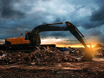 Ein Bagger hebt Schutt unter einem bewölkten Himmel bei Sonnenuntergang.