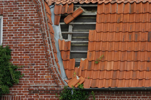 Ein beschädigtes Dach mit fehlenden Ziegeln und einer offenen Stelle an einer Ziegelwand.