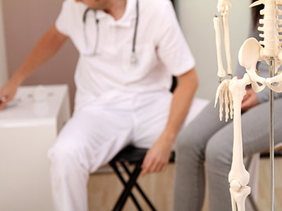 Ein Arzt in weißer Kleidung sitzt neben einem Patienten, während ein menschliches Skelett im Vordergrund steht.