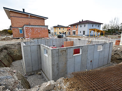 Baugrube mit einer Fertigteilkellerwand und umliegenden unvollendeten Häusern.