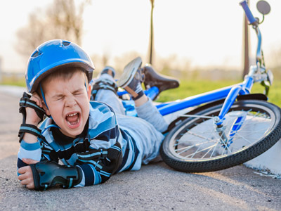 Ein Junge liegt auf dem Boden, weint und hält sich das Ohr, während ein blauer Fahrrad neben ihm steht.