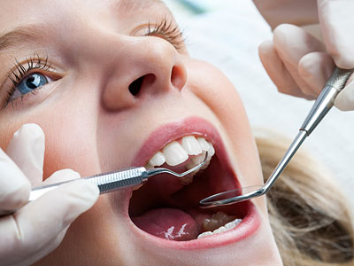 Ein Zahnarzt untersucht das offene Maul eines Patienten mit zahnärztlichem Werkzeug.