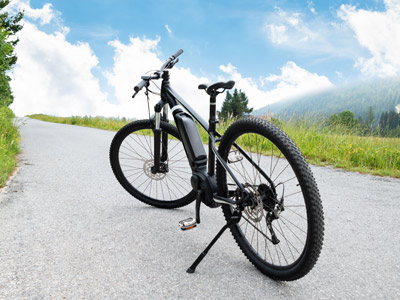 Ein E-Bike auf einer Straße mit grünem Gras und Bäumen im Hintergrund.