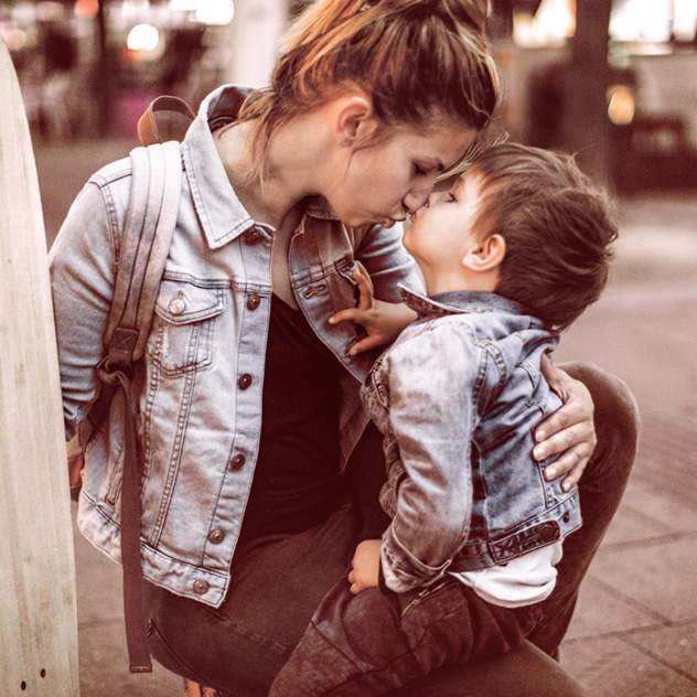 Eine Mutter und ihr Sohn küssen sich, beide tragen Jeansjacken.