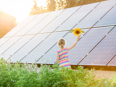 Ein Mädchen mit einem Sonnenblumenstrauß steht vor Solarpanels.