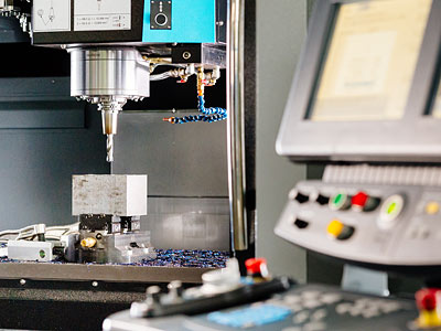 Eine CNC-Fräsmaschine mit einem Bohrer, der ein Werkstück bearbeitet, sowie einem Bedienfeld mit Steuerungselementen.