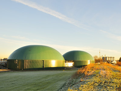 Zwei grüne Biogasanlagen im Freien, umgeben von Gras und bei Morgenlicht.