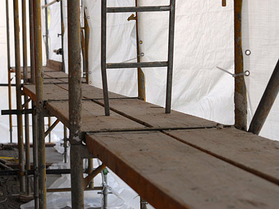Ein Gerüst mit Holzplatten und einem weißen Tuch im Hintergrund.