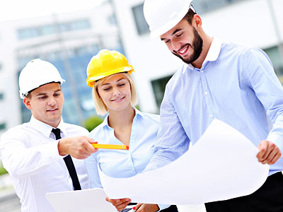 Drei Bauarbeiter besprechen einen Plan. Zwei Männer tragen Sicherheitshelme, während eine Frau einen gelben Helm hat.