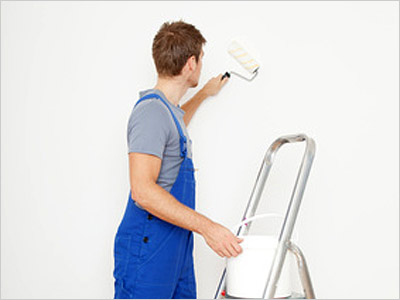 Ein Mann streicht eine Wand mit einer Farbrolle, während er auf einer Leiter steht.