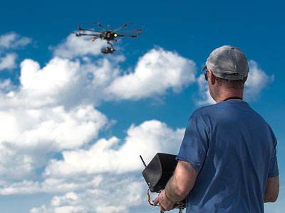 Ein Mann steuert eine Drohne mit einer Fernbedienung, während sie über einem wolkenbedeckten Himmel fliegt.