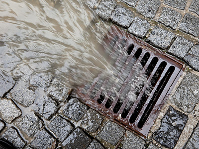 Wasser fließt in einen Gully auf einem gepflasterten Boden.