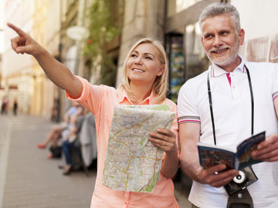Ein Paar steht auf der Straße, hält eine Karte und schaut in verschiedene Richtungen. Die Frau zeigt mit dem Finger nach vorne.