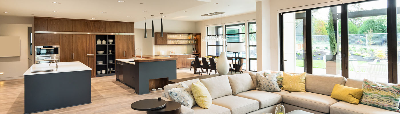 Moderne, helle Küche mit Holz- und grauen Schränken, Insel und Essbereich. Gemütliches Wohnzimmer mit beigem Sofa und bunten Kissen. Große Fenster mit Blick auf den Garten.