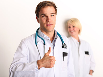 Ein Arzt gibt ein Daumen-hoch-Zeichen, während eine weitere Person im Hintergrund lächelt.