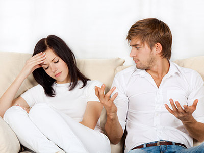 Ein Paar sitzt auf einer Couch. Die Frau sieht frustriert aus, während der Mann gestikuliert und spricht.
