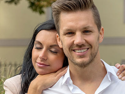 Ein Paar lächelt miteinander, die Frau lehnt sich an den Mann.