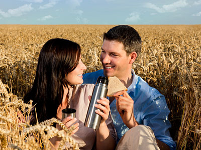 Ein Paar sitzt in einem Weizenfeld und genießt ein Picknick mit einer Thermoskanne und einem Sandwich.