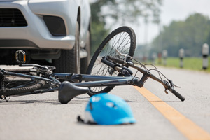 Ein verunfalltes Fahrrad und ein blauer Helm liegen auf der Straße, in der Nähe eines Autos.