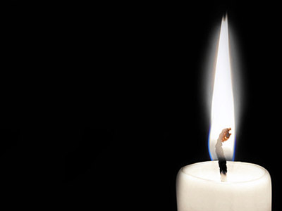 Eine brennende Kerze vor schwarzem Hintergrund.