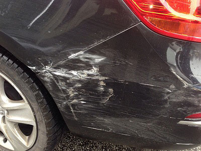 Ein beschädigter schwarzer PKW mit Kratzern an der hinteren Stoßstange.