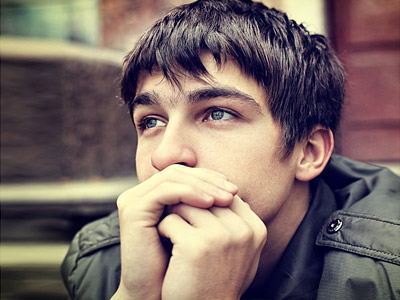 Ein nachdenklicher Jugendlicher mit kurzem Haar, der seine Hände vor dem Gesicht hält.
