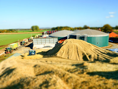 Eine Ansicht einer landwirtschaftlichen Anlage mit Lagerhallen, Fahrzeugen und einem großen Haufen von Materialien im Vordergrund.