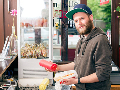 Ein Mann in einem Restaurant, der Hotdogs zubereitet und Ketchup sowie Senf in der Hand hält.
