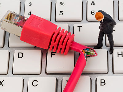 Ein kleiner Mann steht neben einem beschädigten, pinken Ethernet-Kabel, das auf einer Tastatur liegt.