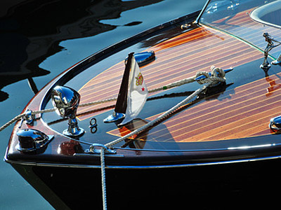 Ein Holzboot mit einem weißen Flaggenmast, glänzenden Beschlägen und einem Seil, das am Bug befestigt ist.