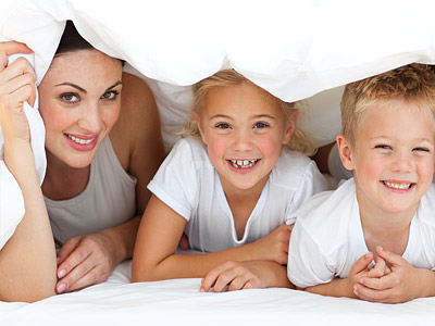 Eine Frau und zwei Kinder liegen unter einer Decke und lächeln.