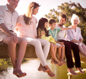 Eine Gruppe von Menschen sitzt barfuß auf einem Steg über einem Gewässer und genießt die Zeit miteinander.