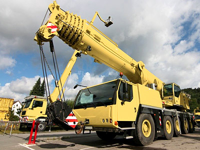 Ein gelber Kran steht auf einem Parkplatz unter einem bewölkten Himmel.