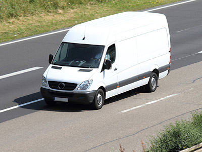 Ein weißer Lieferwagen fährt auf einer Landstraße.