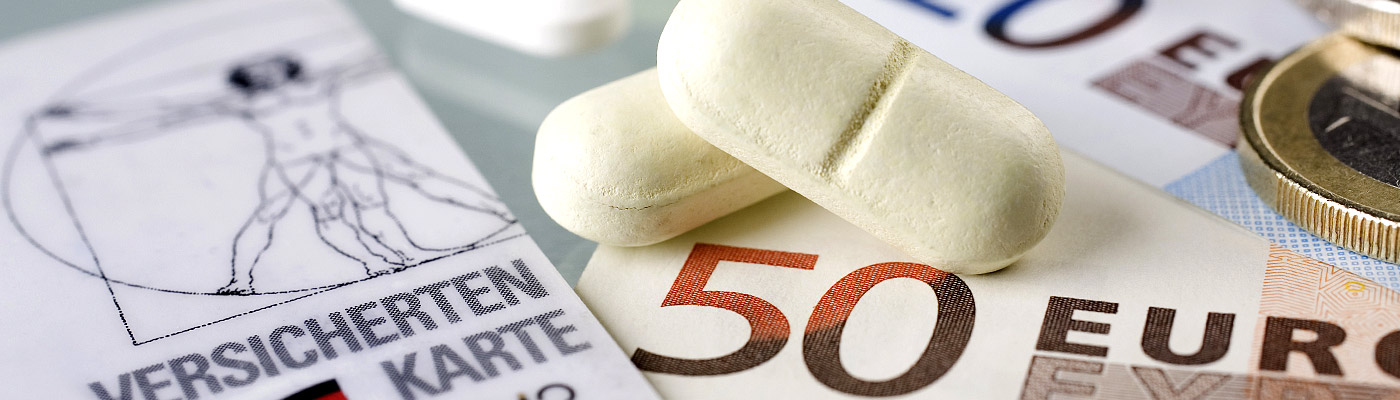 Auf dem Bild sind zwei weiße Tabletten, eine Gesundheitskarte mit dem Schriftzug "VERSICHERTENKARTE" und ein 50-Euro-Schein sowie einige Münzen zu sehen.