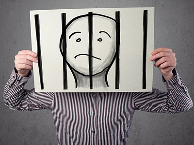Eine Person hält ein Plakat mit einem traurigen Gesicht hinter Gittern.