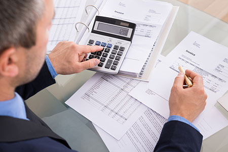 Ein Mann verwendet einen Taschenrechner und notiert etwas auf Papiere mit Rechnungen auf einem Tisch.