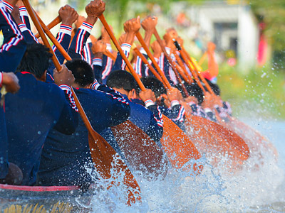 Ein Team von Paddlern im Boot, die synchron mit ihren Paddeln im Wasser schlagen. Wassertropfen spritzen.