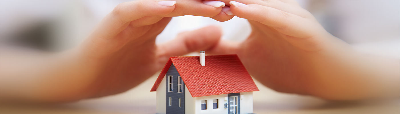 Zwei Hände schützen ein kleines Modellhaus.
