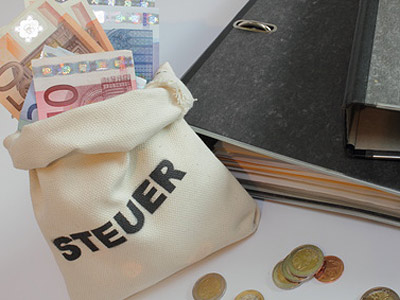 Ein Geldsack mit Euro-Scheinen und Münzen, daneben ein Aktenordner.