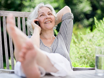 Eine lächelnde ältere Frau entspannt sich auf einer Terrasse, während sie telefoniert.